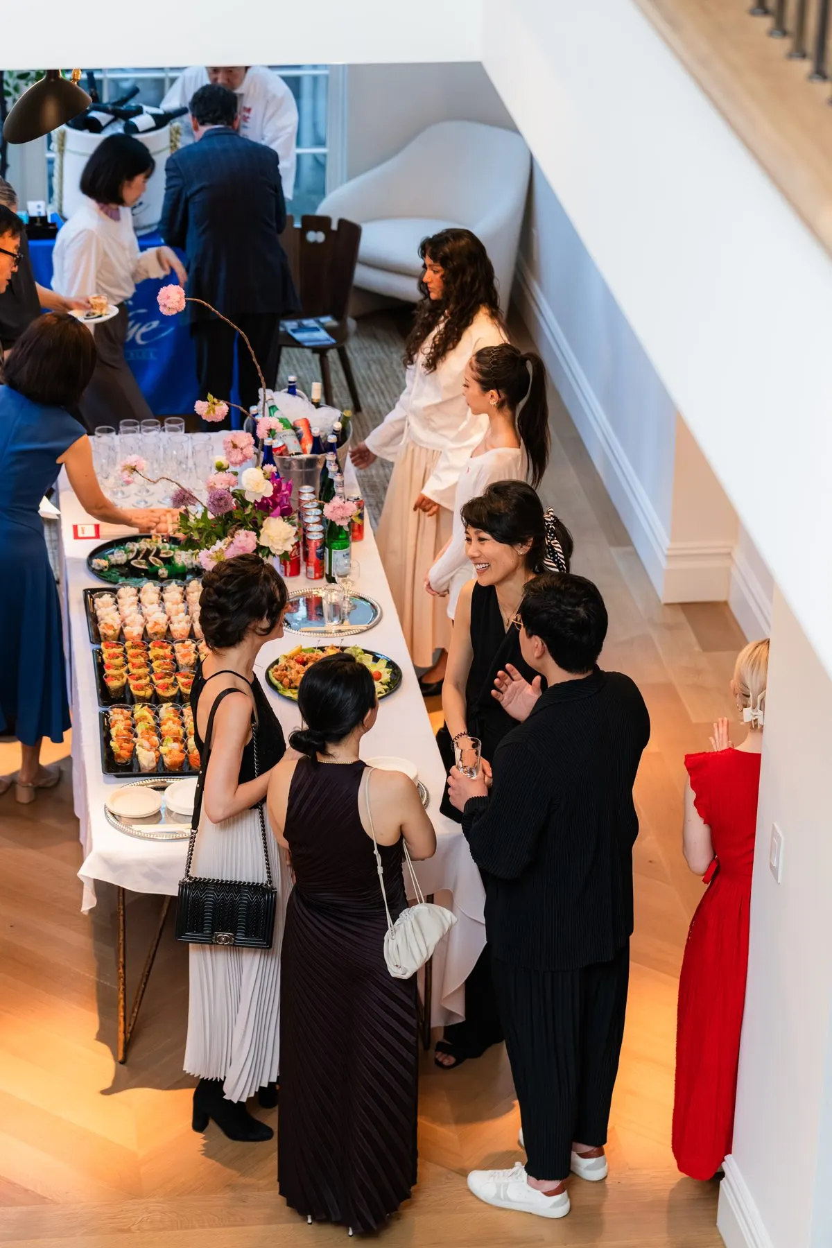 Guests talking around the food and sake table at the townhouse, seen from the stairs