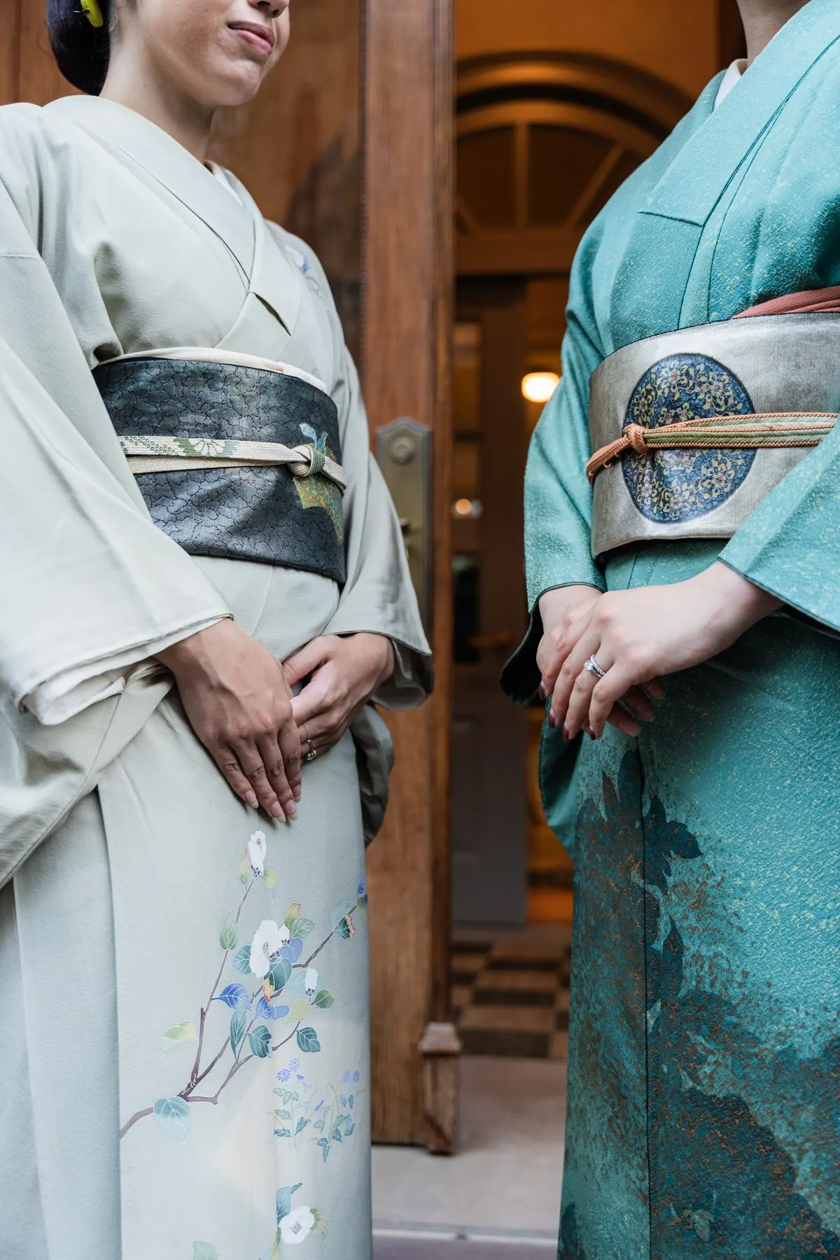 Two hosts in kimono at the townhouse door, hands folded over their obi