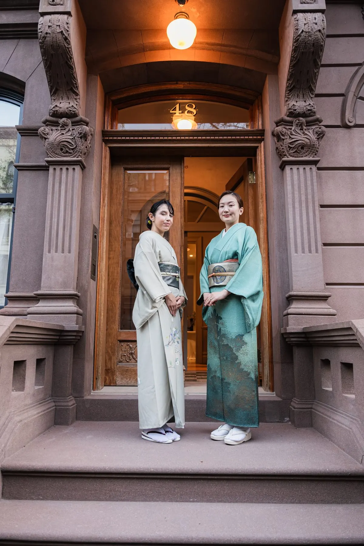 Two hosts in kimono in the open front door of the townhouse